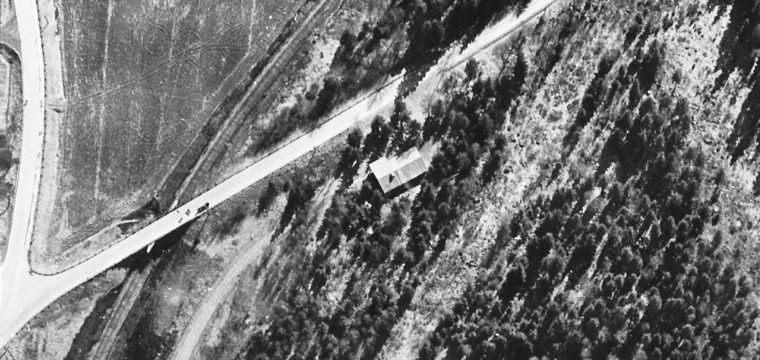 Taket på Kruschens kiosk syns svagt i bildens nedre vänstra hörn mot vägen. Huset i bildens mitt är scoutstugan. Flygfoto från 1959